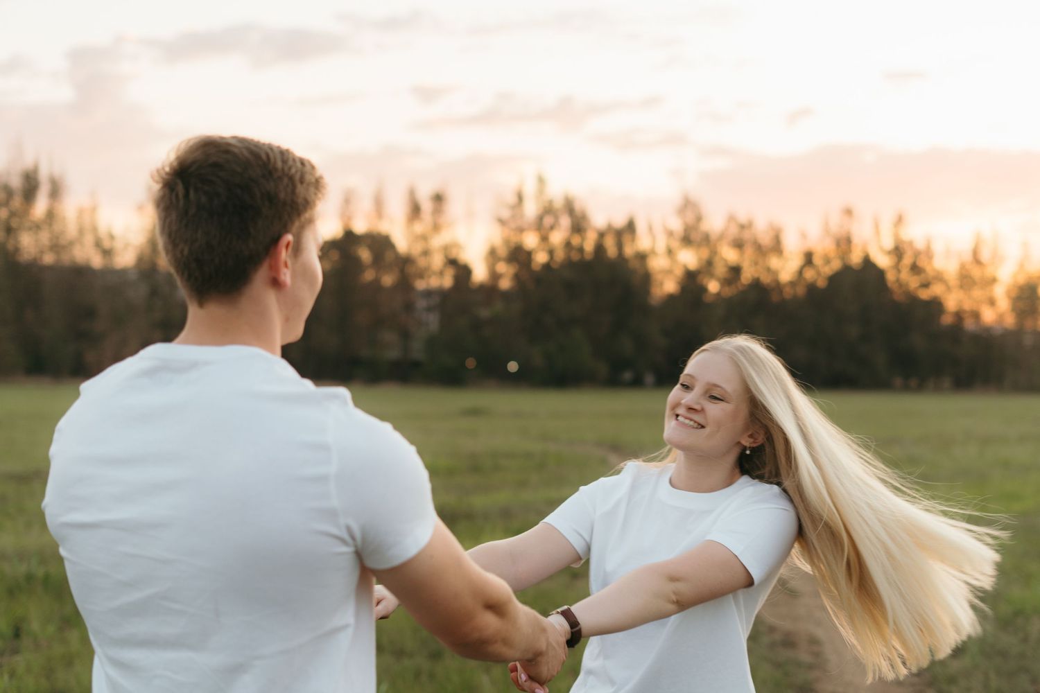 Couple in matching white outfits dancing together in a field at golden hour.