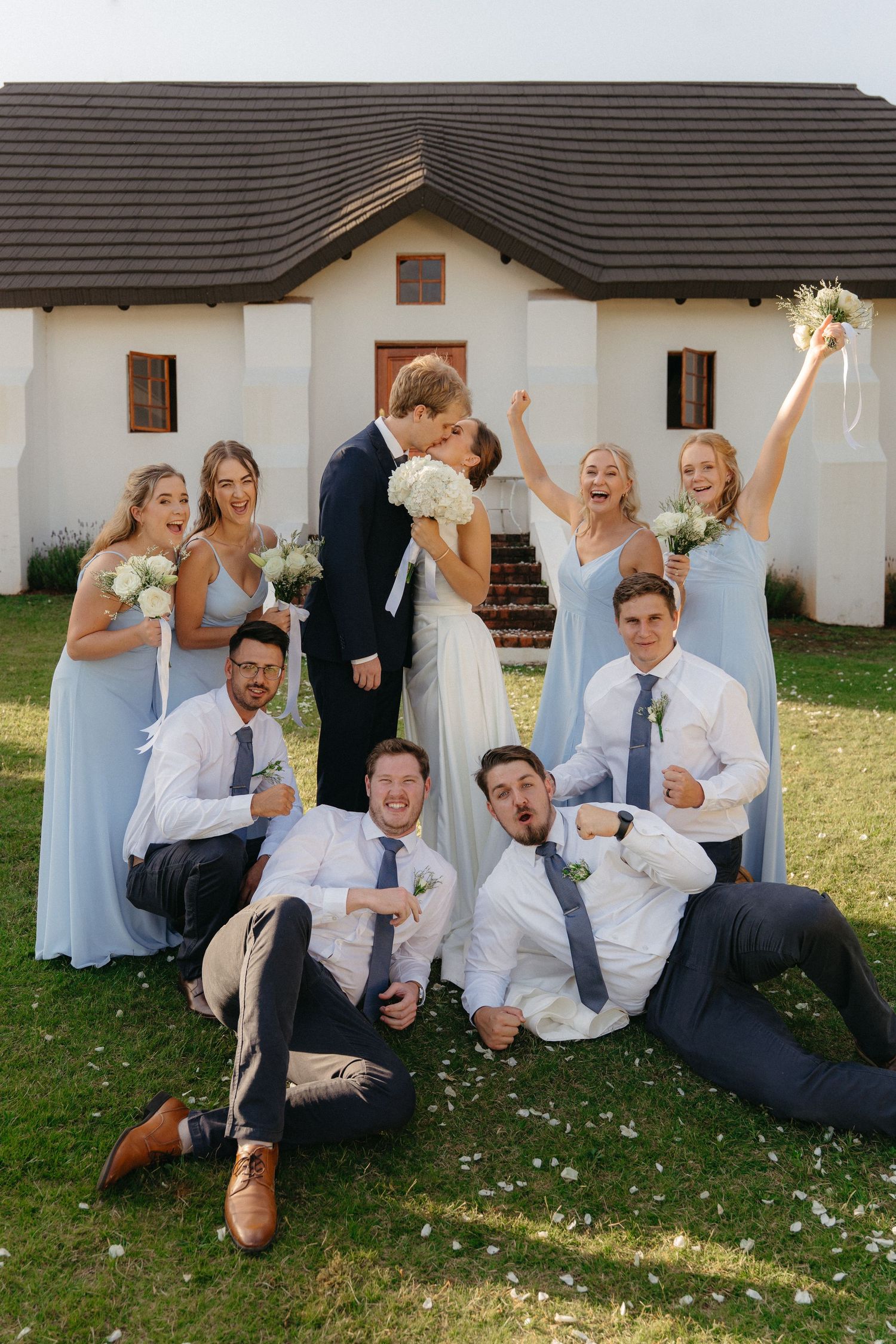 A playful wedding party poses on the grass in a sequence of candid shots showing joyful interactions.