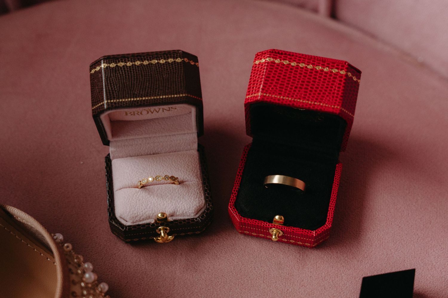 Close-up view of wedding rings displayed in elegant red and black jewelry boxes on a soft pink surface.