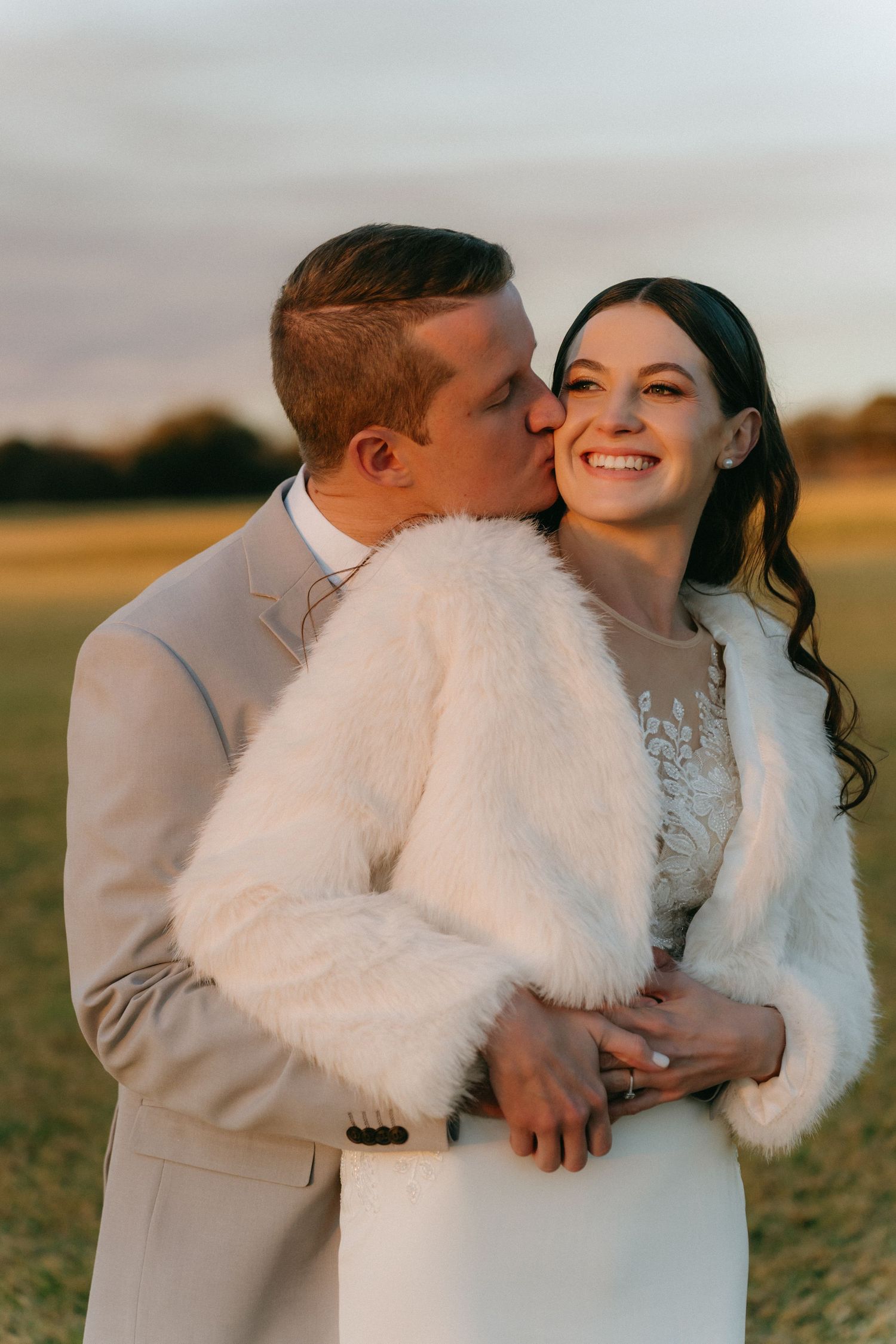 A couple shares intimate moments in a winter field at sunset wearing white winter wedding attire.