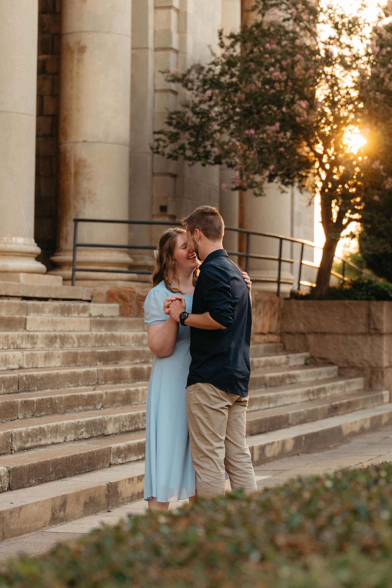 A romantic couple shares tender moments on stone steps at sunset with classical columns in the background.