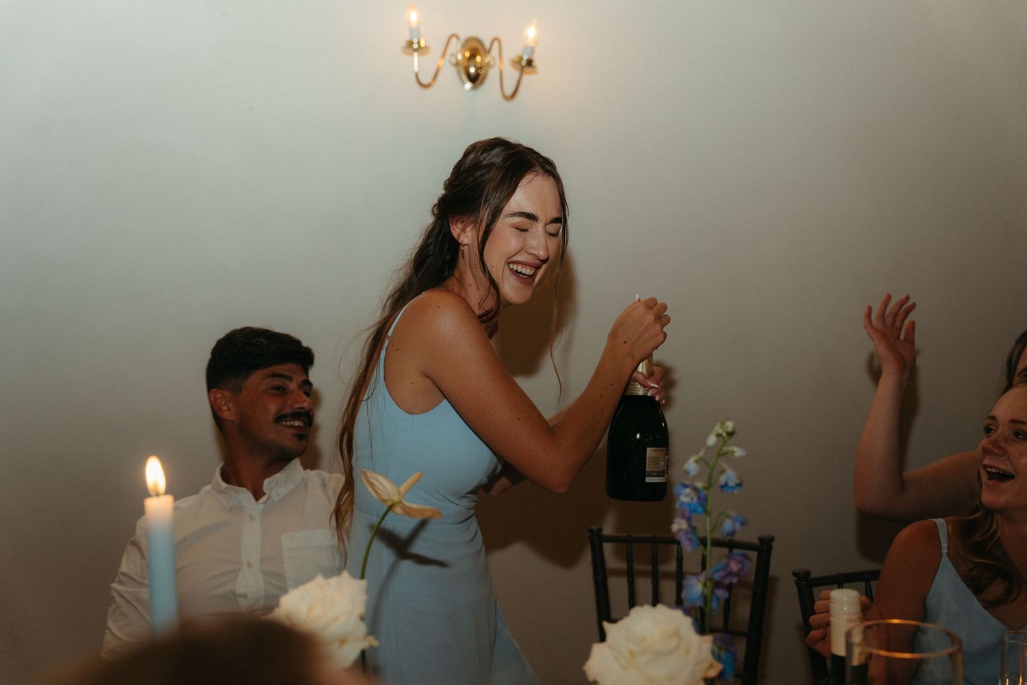 Wedding reception celebration with guests dancing under warm candlelight and chandeliers.
