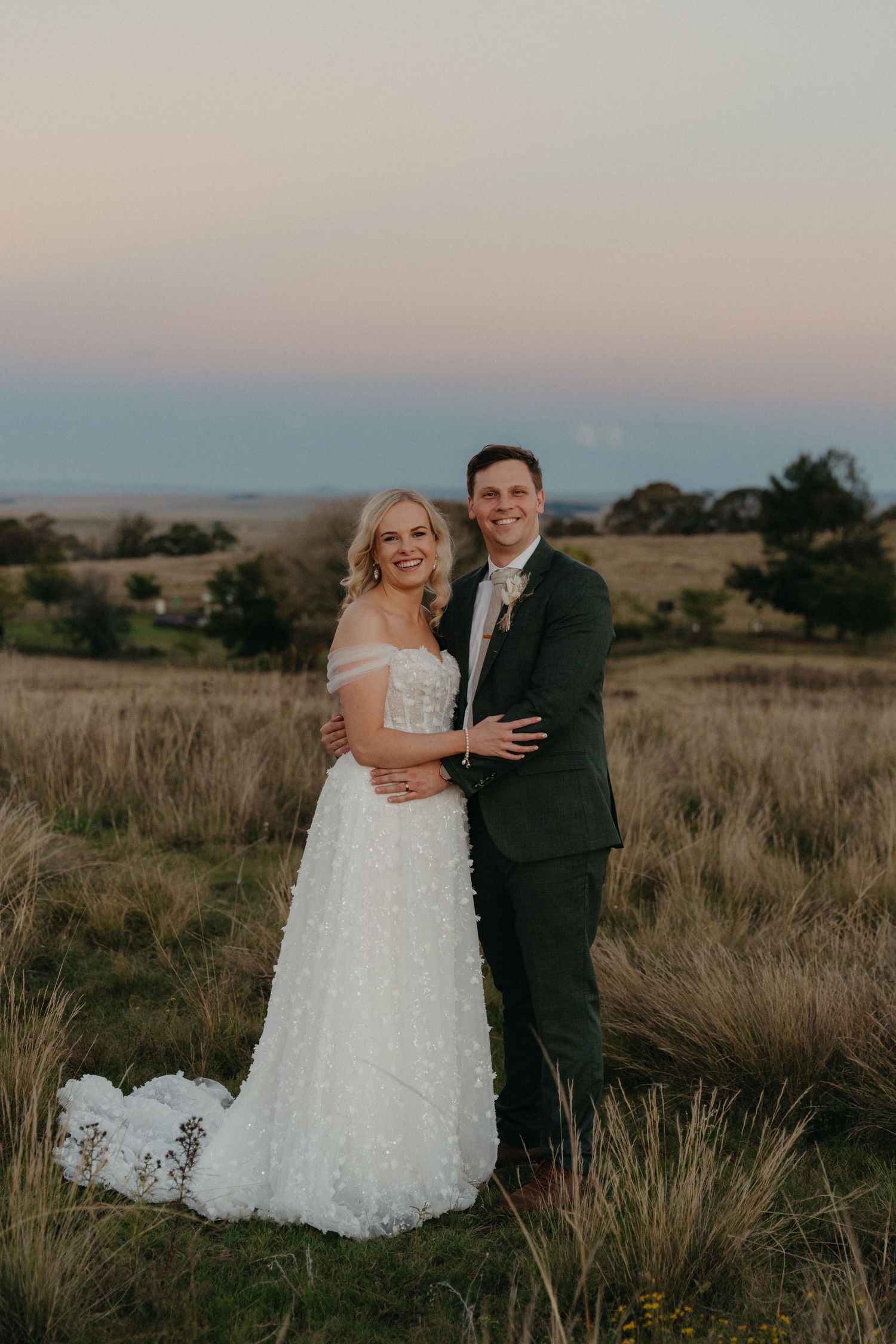 Happy bride and groom posing in open Free State field at sunset with pastel sky.