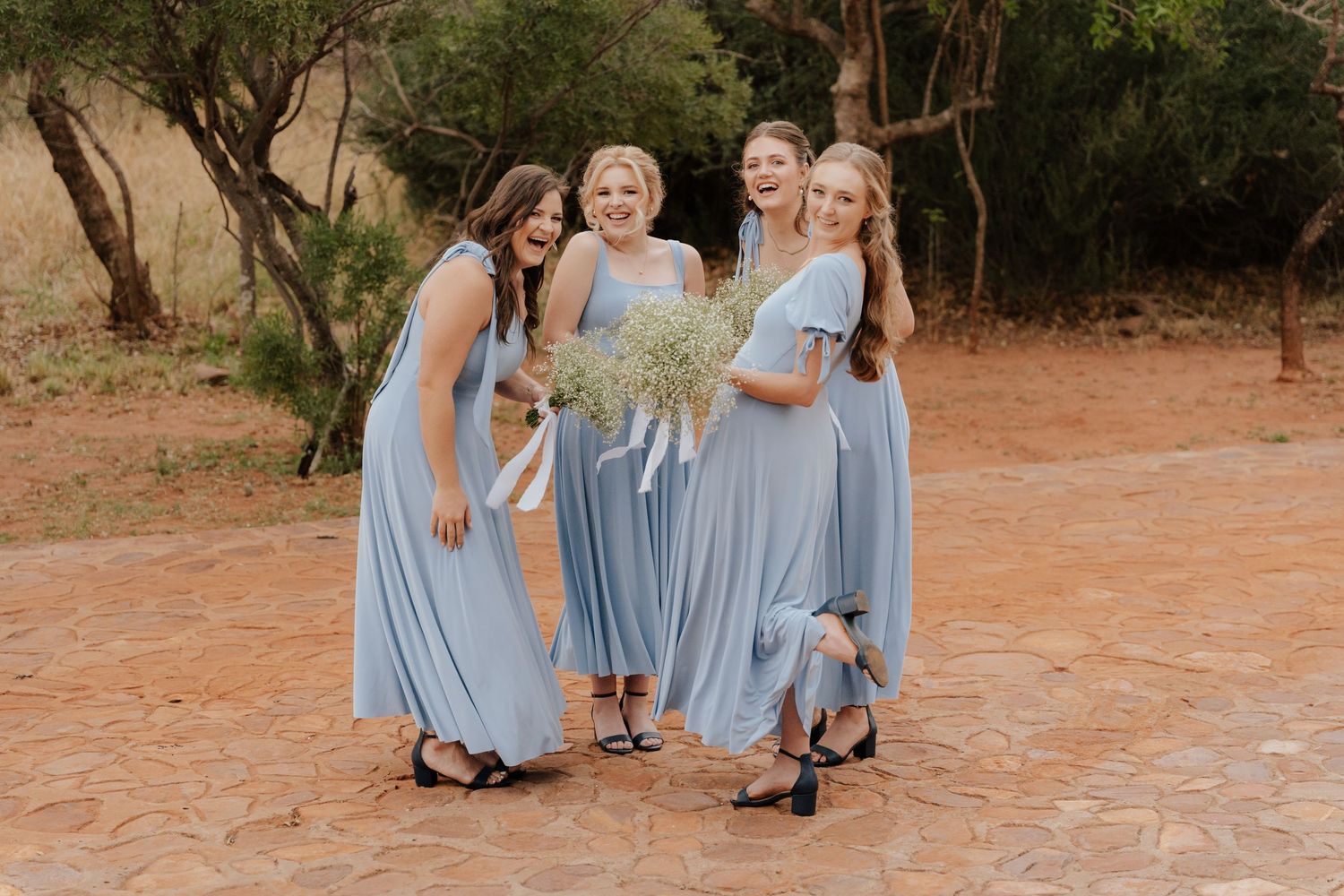 Bridesmaids in light blue dresses pose together outdoors.