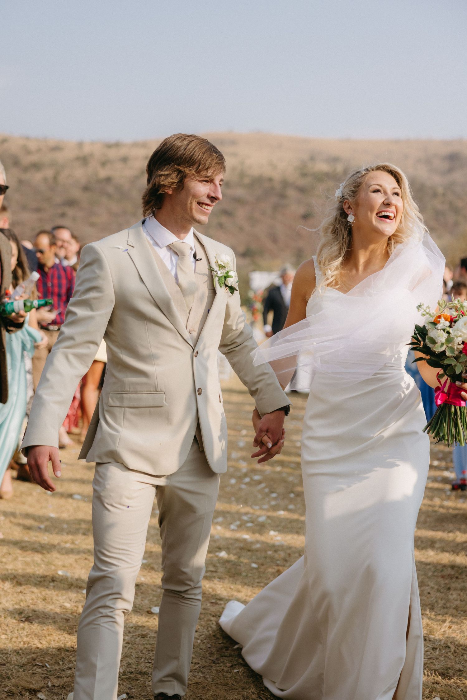 Newlyweds share a joyful dance together outdoors in a desert setting wearing white and beige attire.