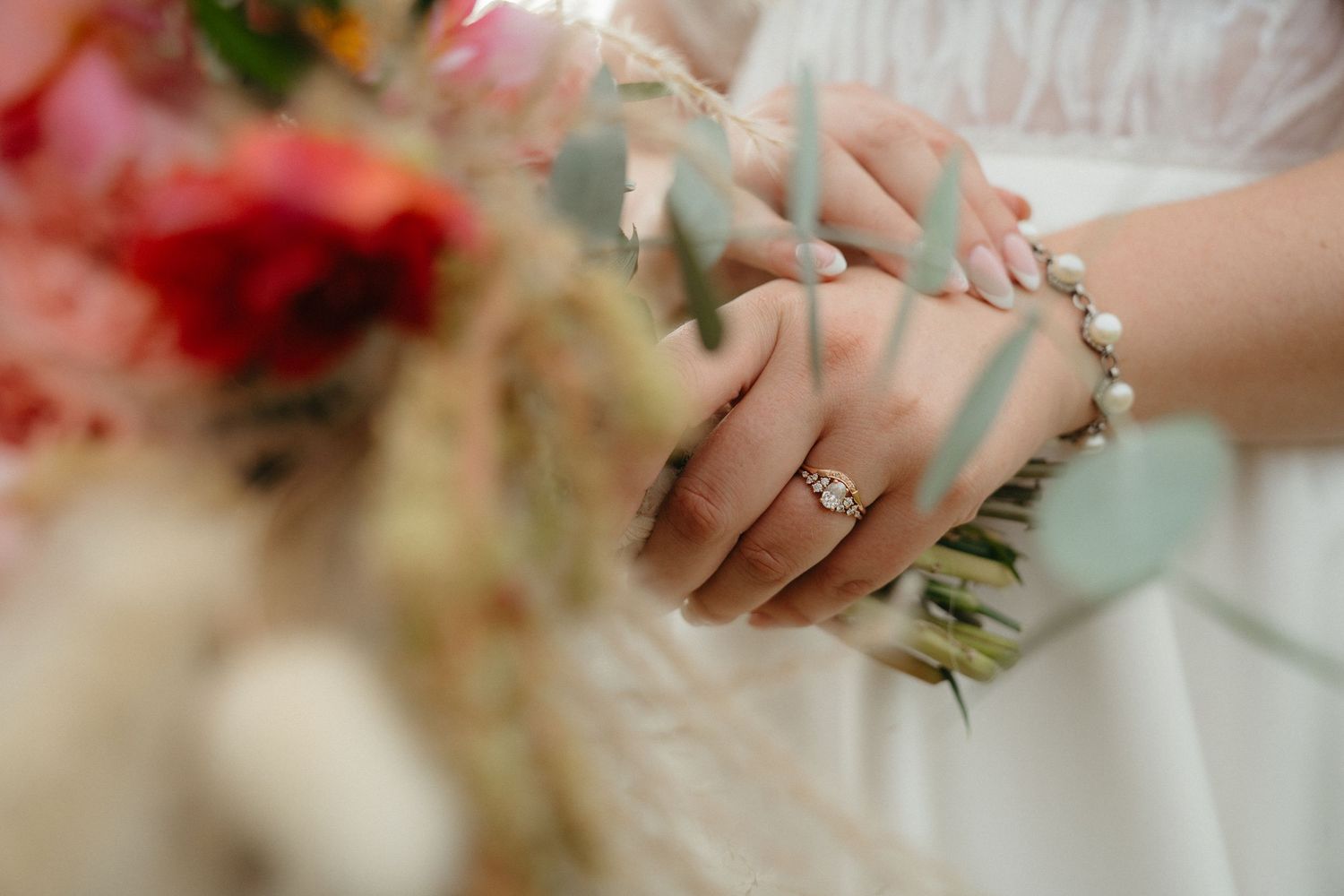 Close-up detail of hands holding a wedding bouquet with a sparkling engagement ring.