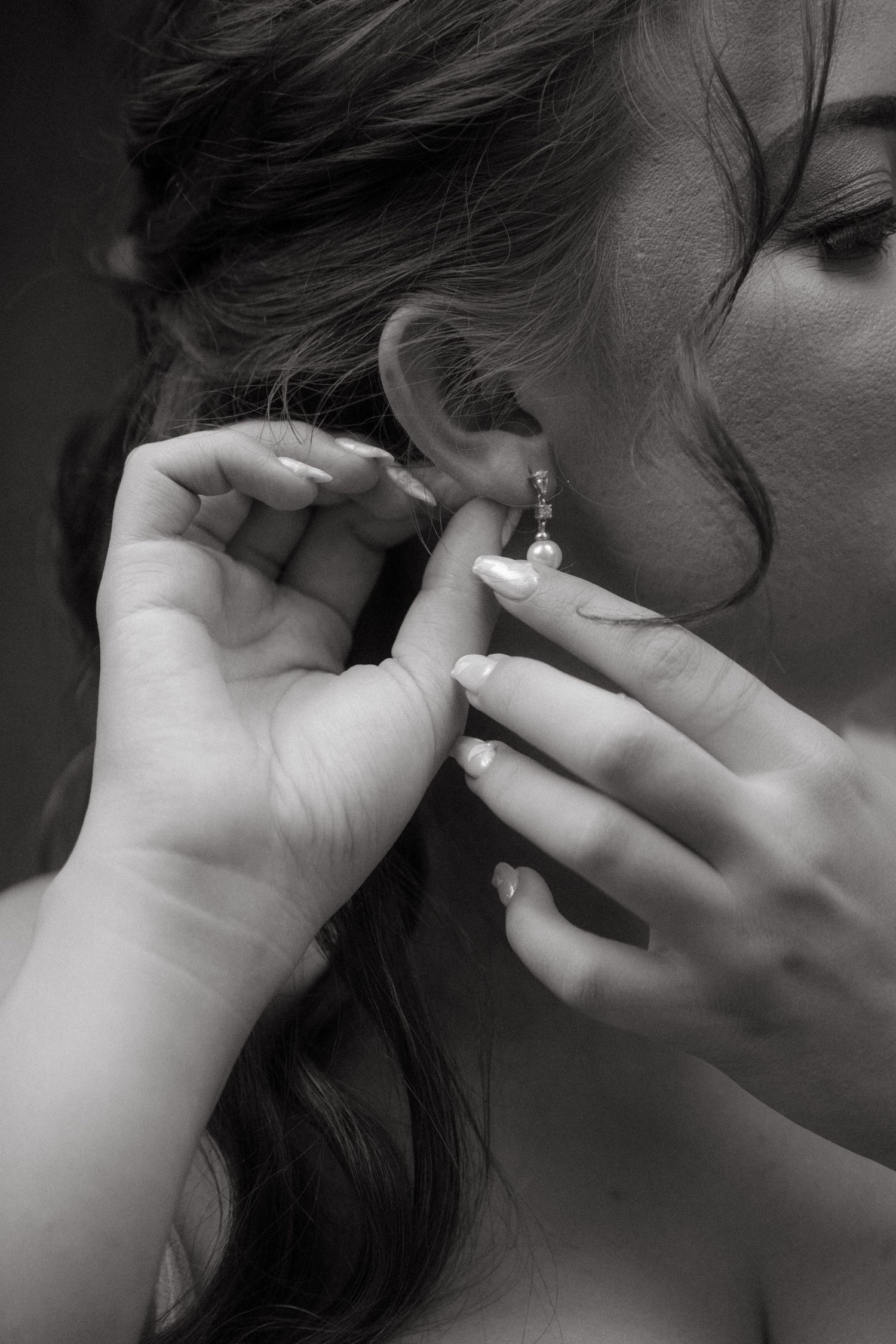 Black and white close-up of hands putting on delicate earring during wedding preparations.