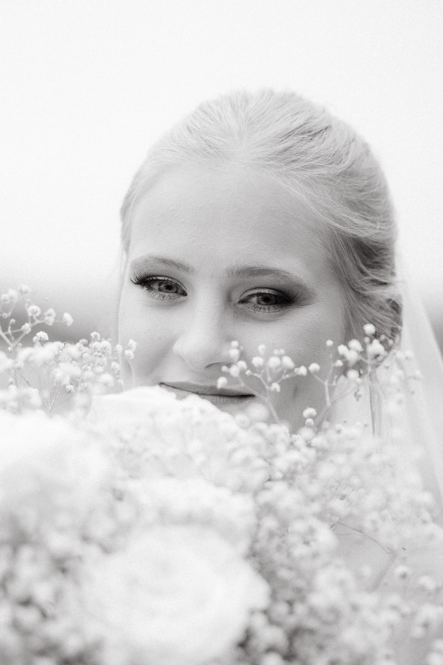 Artistic black and white portrait through delicate white flowers creating a dreamy effect.