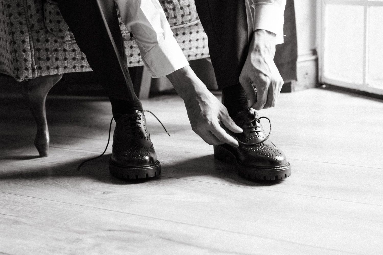 Black and white photo of hands tying formal dress shoes on hardwood floor.