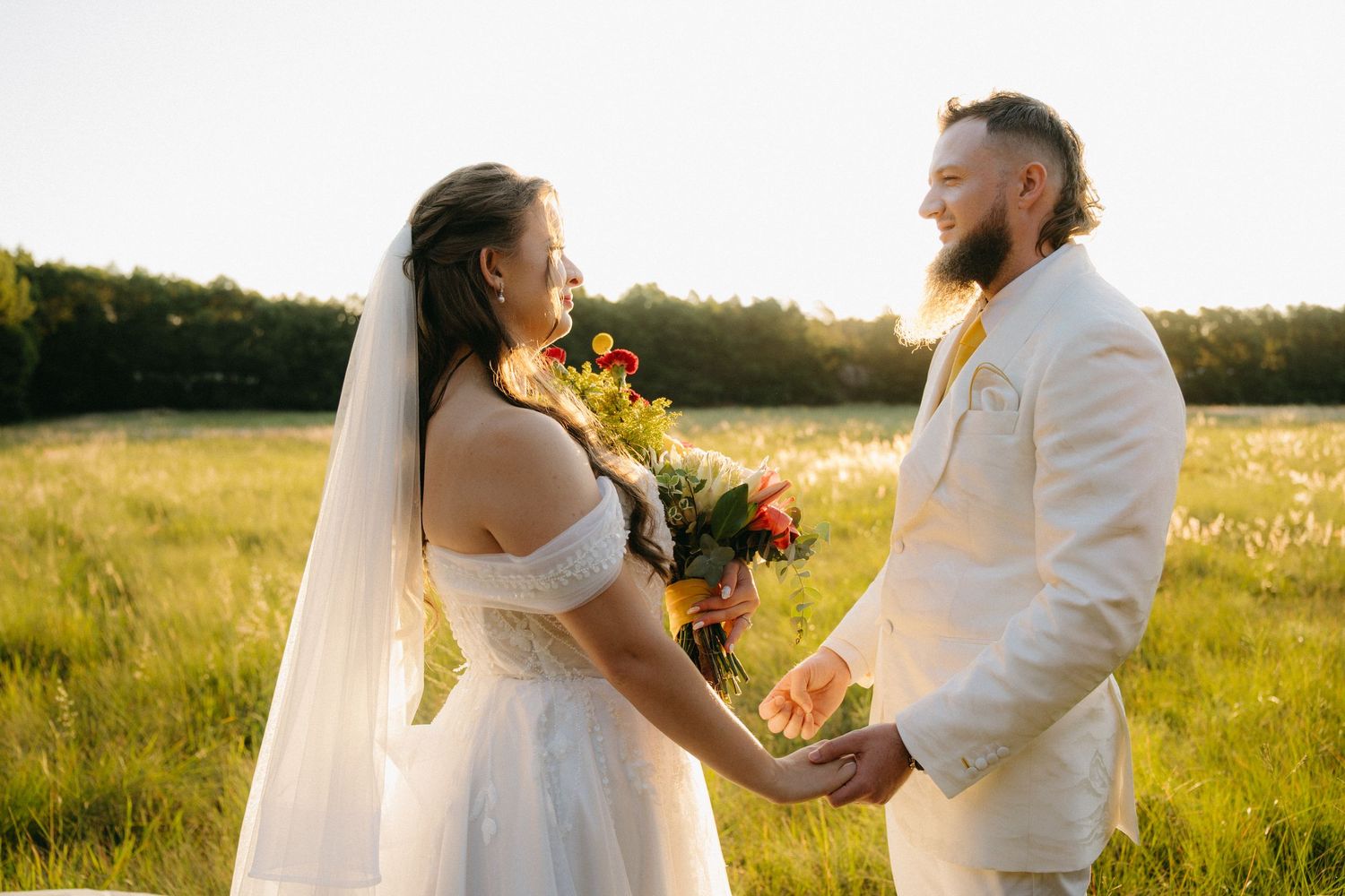 Sunset wedding portrait of couple in white attire holding hands in a golden field.