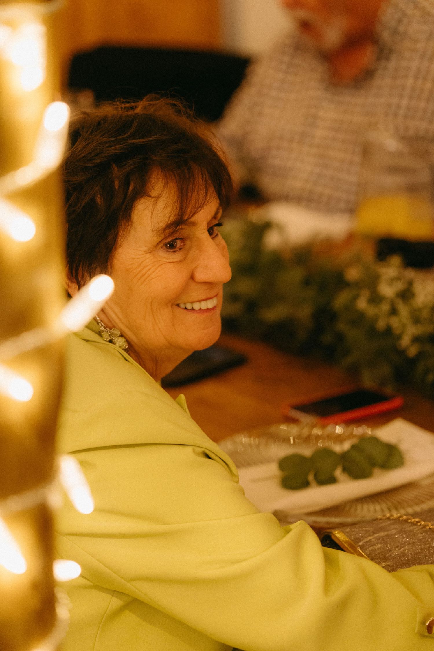 Person in yellow jacket smiles warmly in ambient lighting at an event.