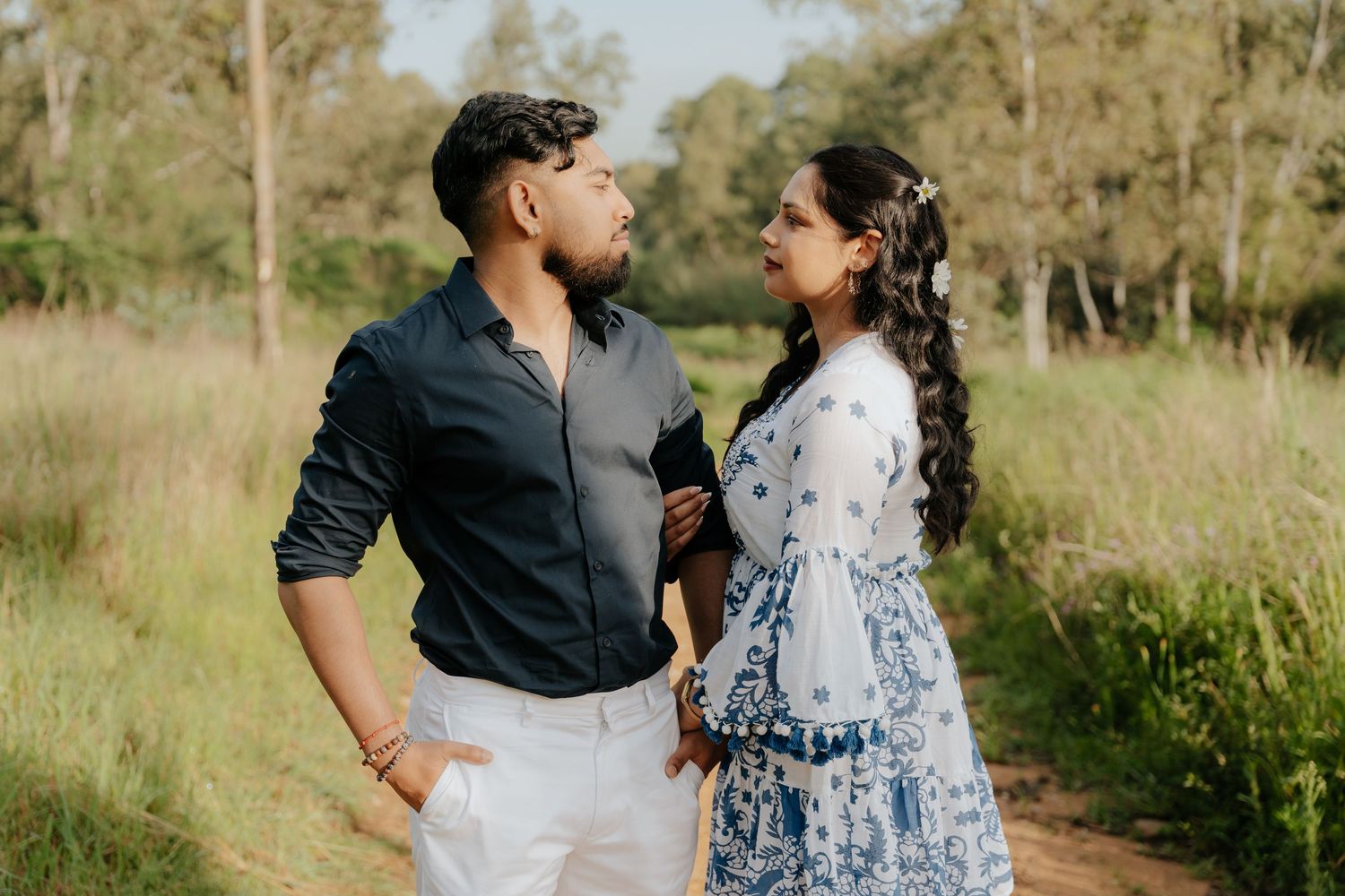 A couple shares a romantic moment on a nature trail surrounded by lush greenery and golden sunlight.