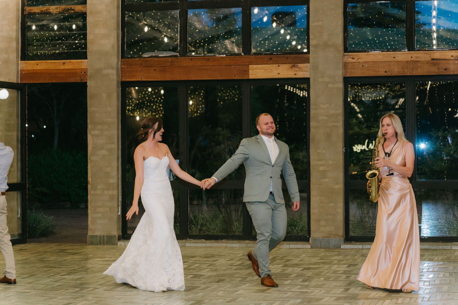 Wedding party dances together in modern indoor venue with glass windows.