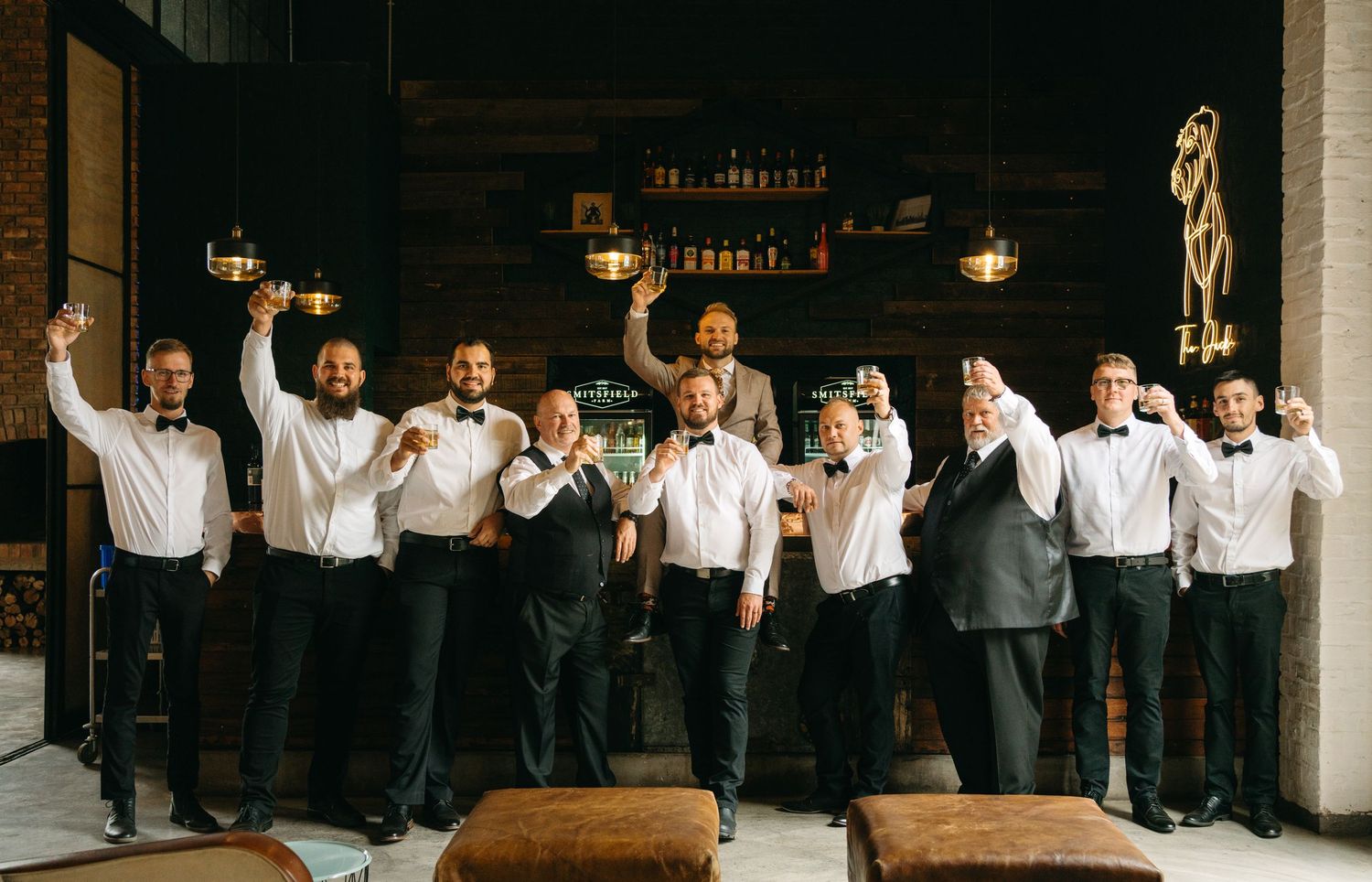 Groomsmen in white shirts and dark pants pose together in a rustic venue.