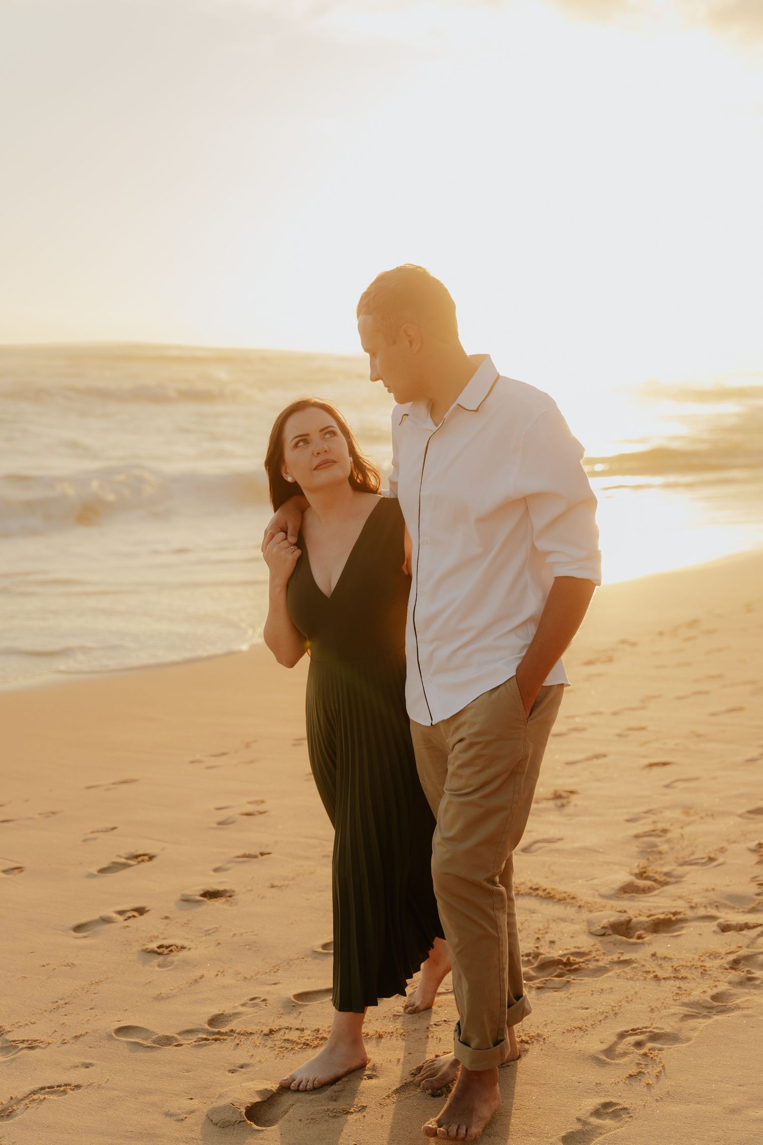 A couple walks along a sandy beach at sunset in warm golden light.