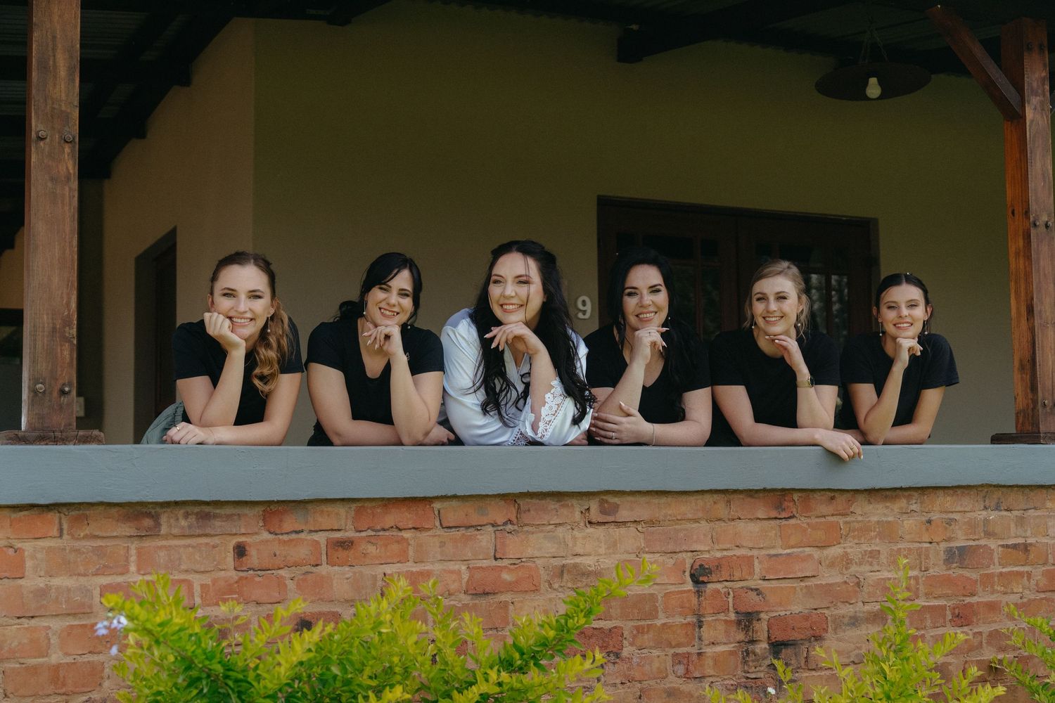 Wedding party members in black dresses posing together on a rustic brick porch ledge.