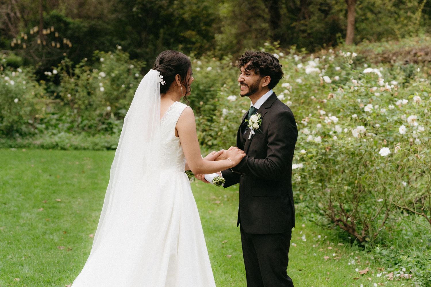 A couple shares a tender moment in a garden setting with blooming white flowers and lush greenery during a wedding celebration.