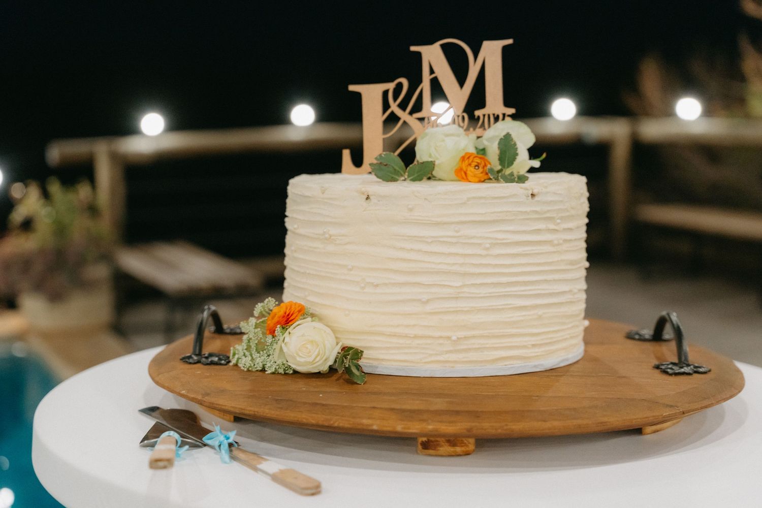Wedding cake display on wooden stand with monogram topper and floral decorations.