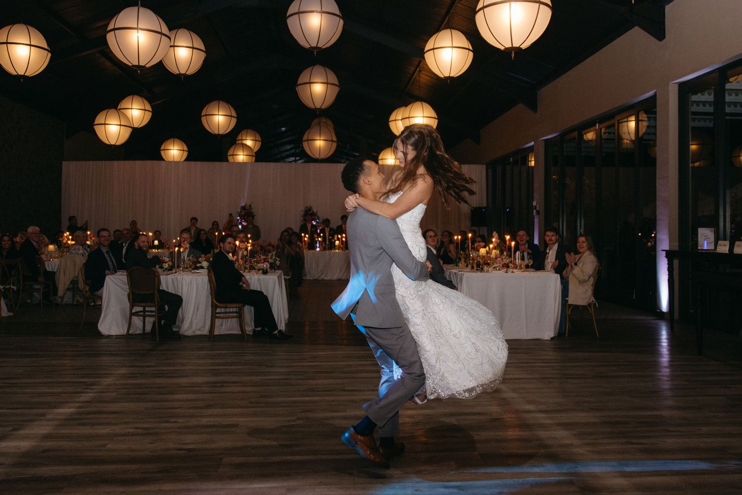 Bride and groom share first dance under glowing lanterns at elegant wedding reception venue.