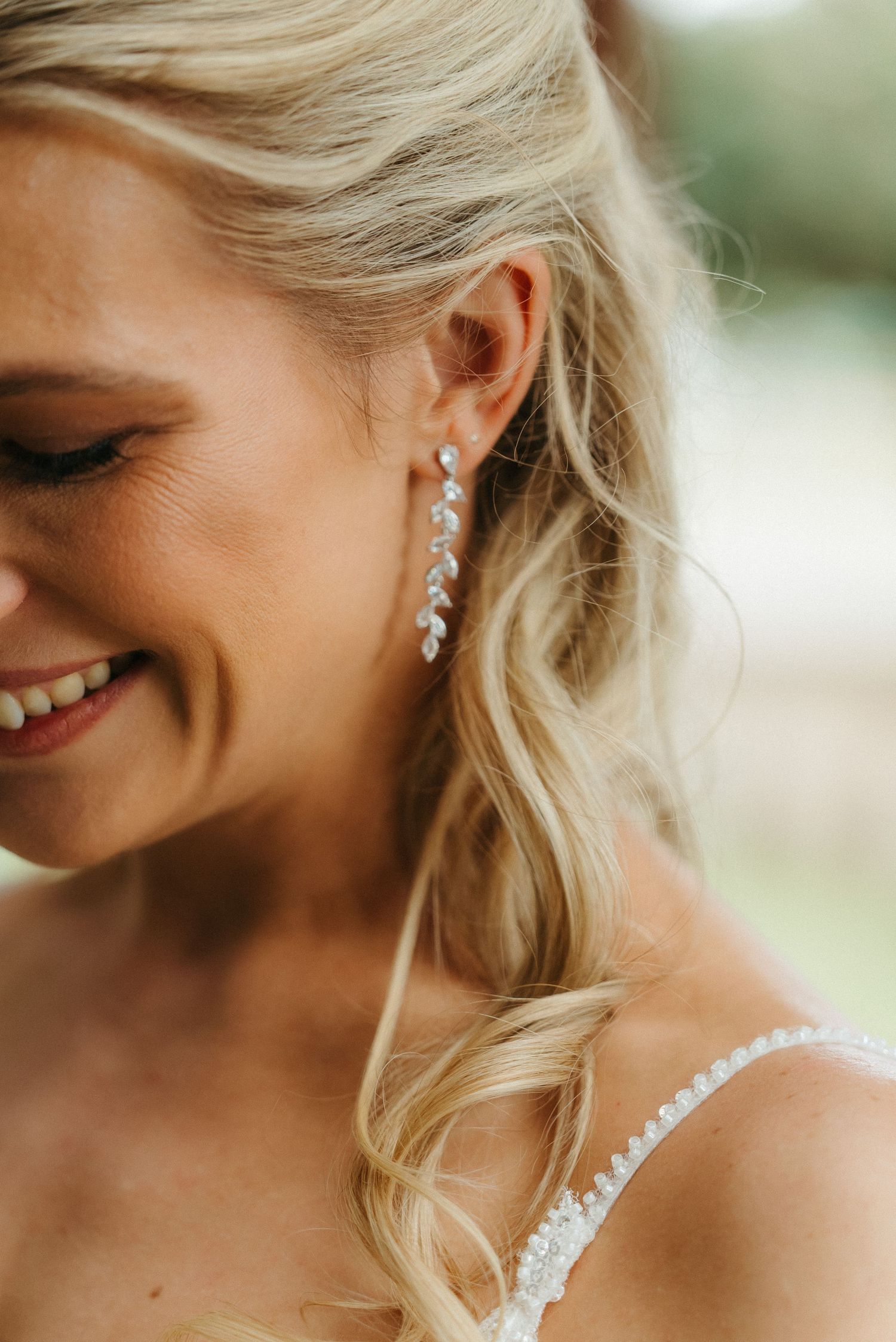 Smiling blonde bride wearing elegant crystal drop earrings with lace dress, close-up portrait shot.