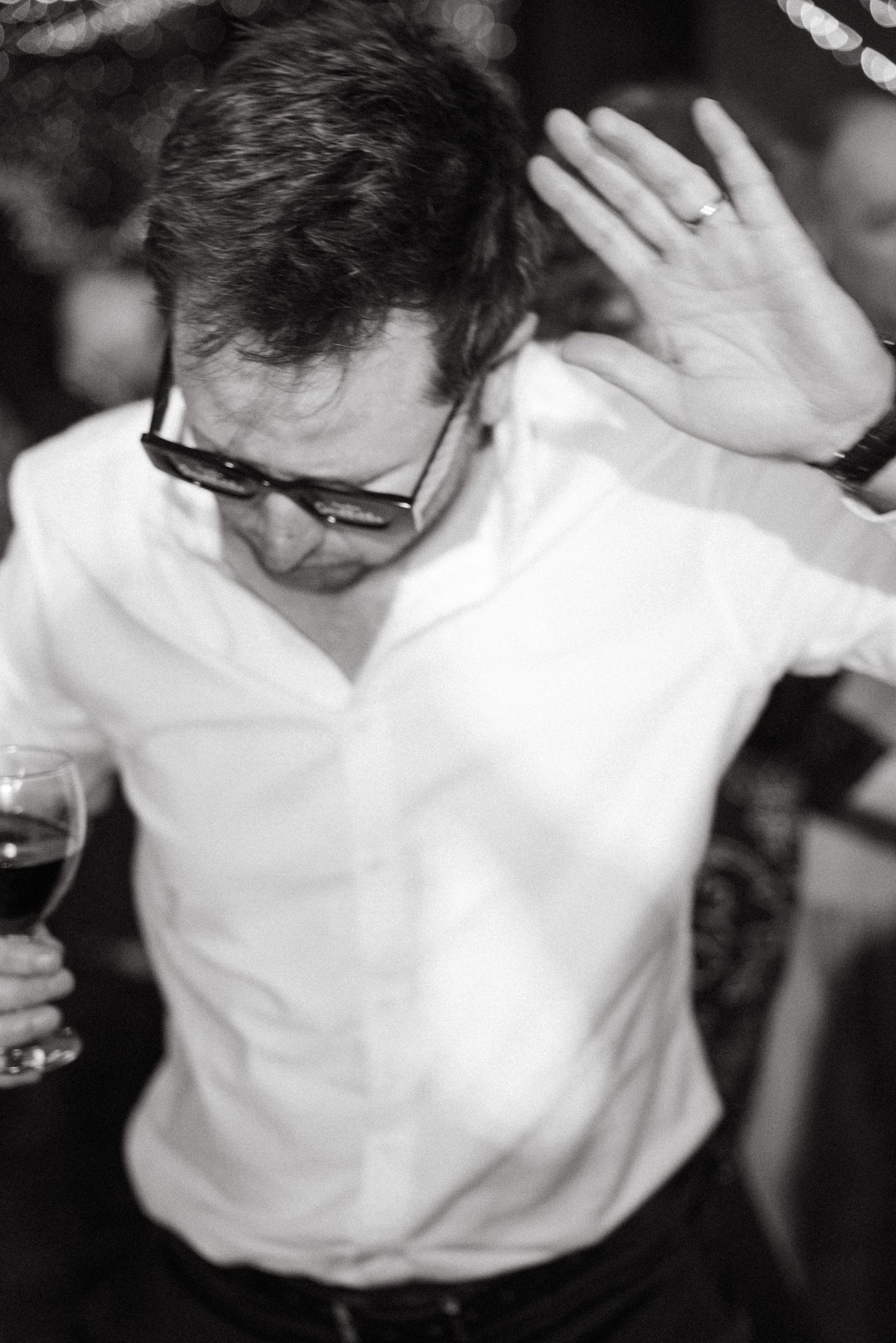 Man in white shirt holding red wine glass, raising hand, wearing sunglasses, black and white party photo.