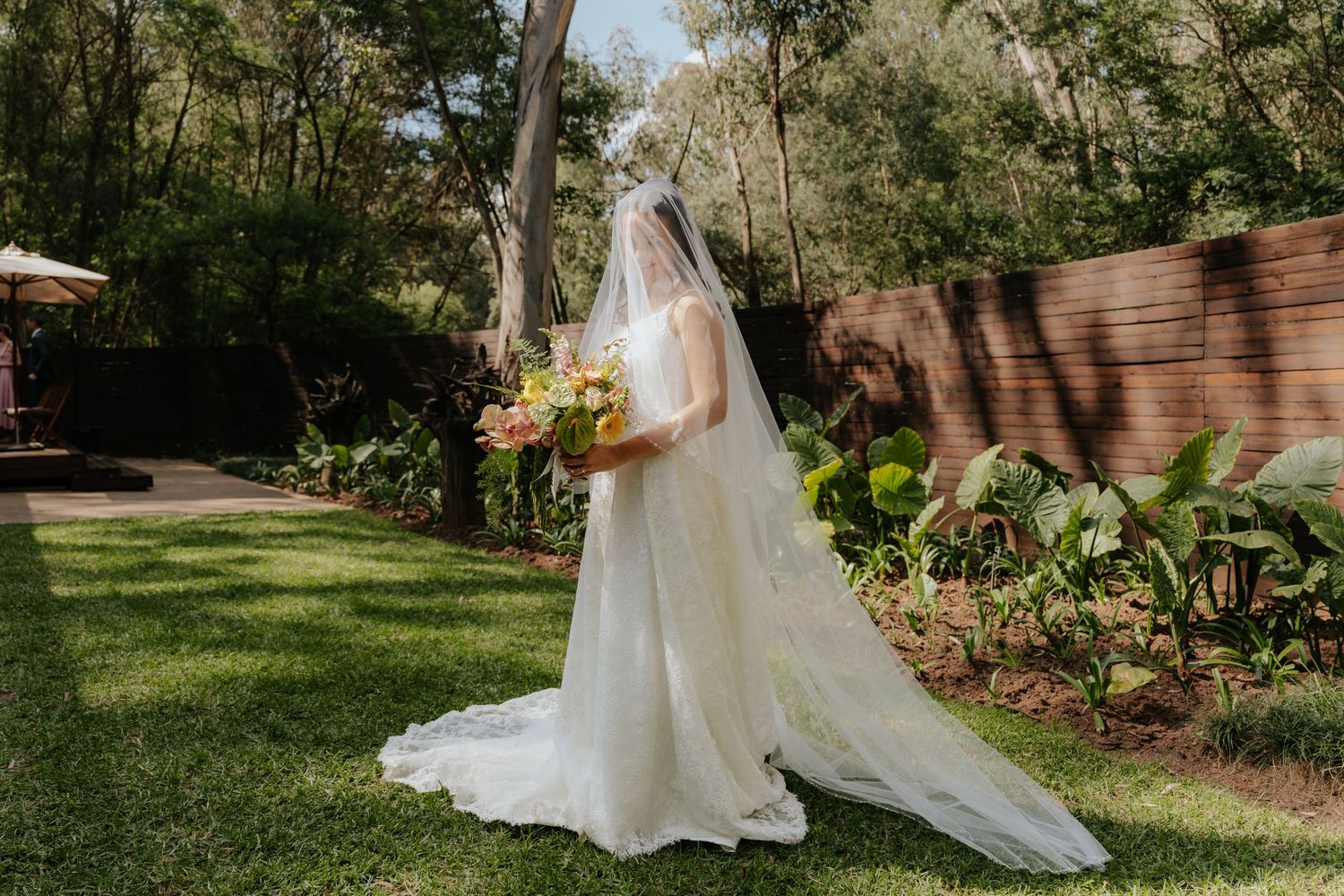 Bride in white gown and cathedral veil holding colorful bouquet in lush garden setting in Mpumalanga