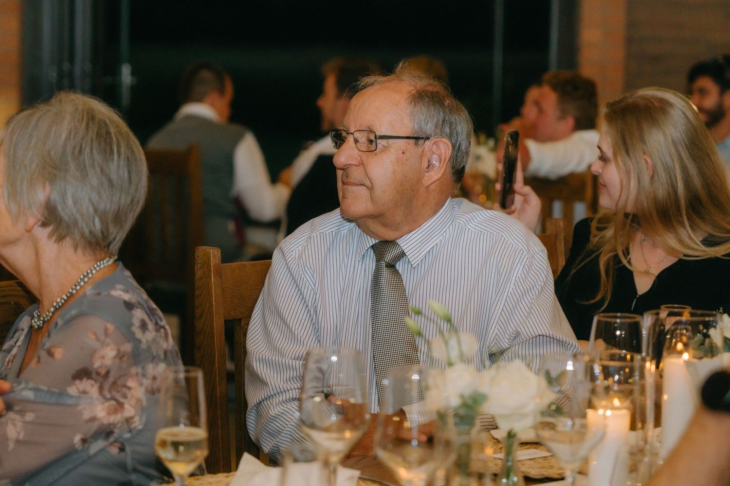 An attendee wearing glasses and a striped shirt enjoys an elegant candlelit dinner reception at a formal event.