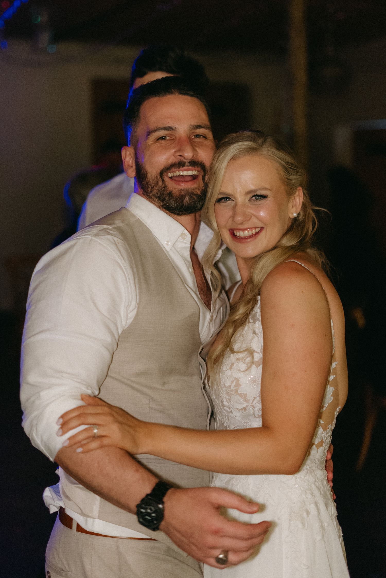 Couple shares joyful dance moments under dim reception lighting.