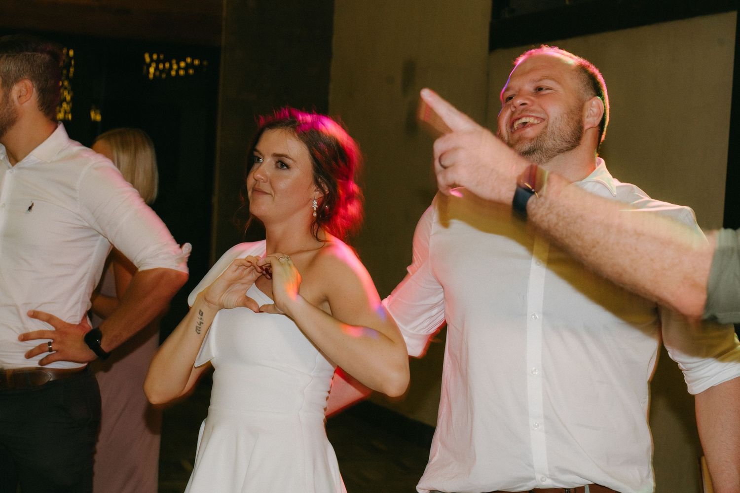 People dance and celebrate at a wedding reception with red lighting effects in the background.