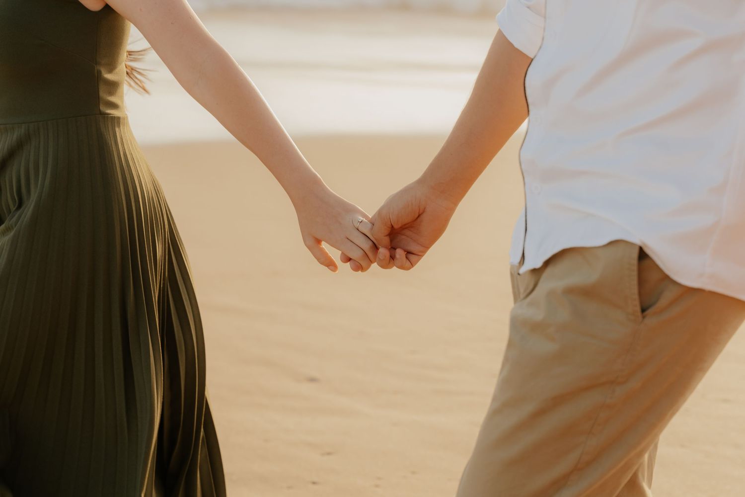 Two people holding hands walk along a sandy beach in the Garden Route at sunset with warm golden light.