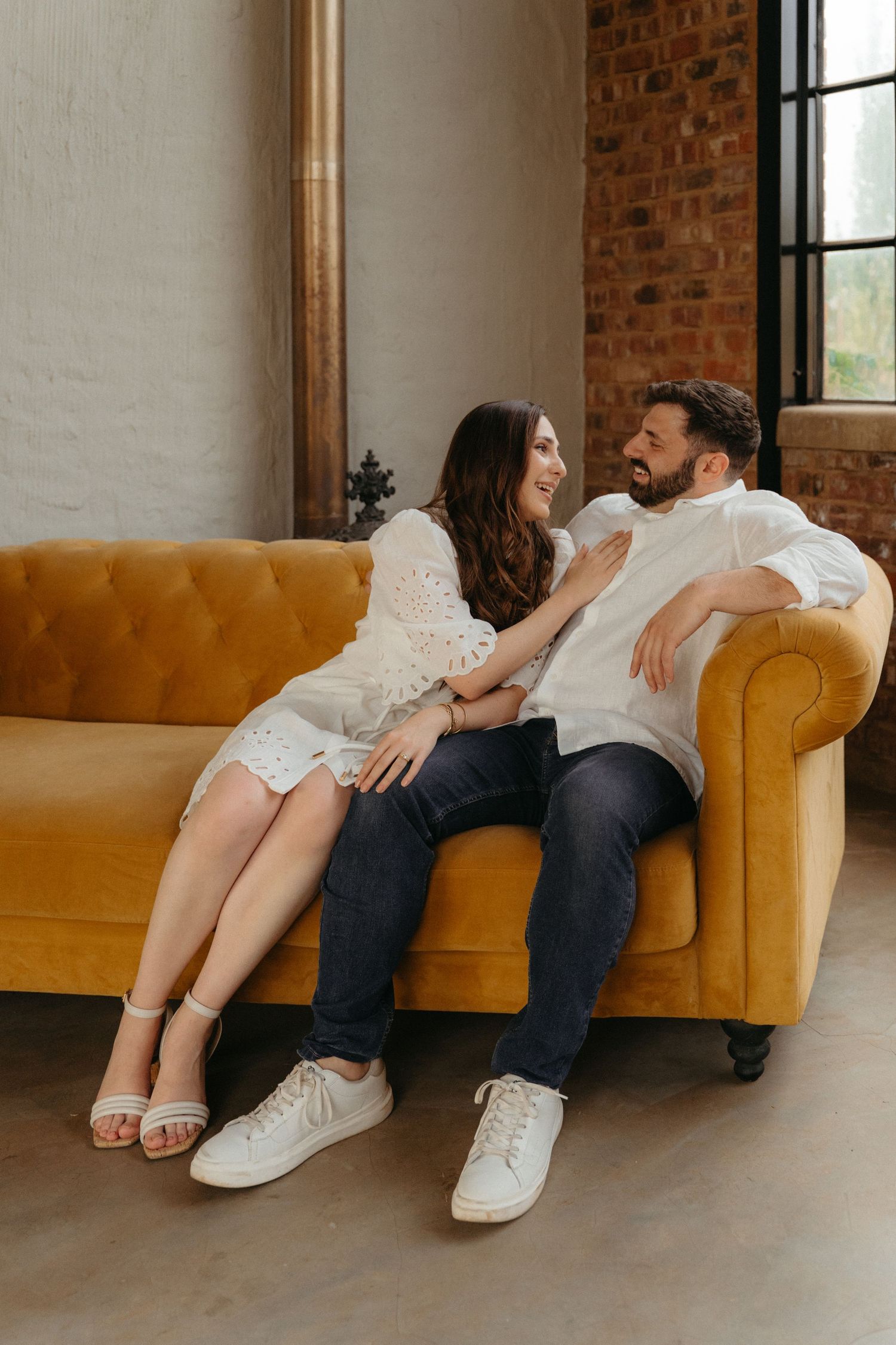 Couple relaxing on mustard yellow velvet sofa in industrial-style room with brick walls.