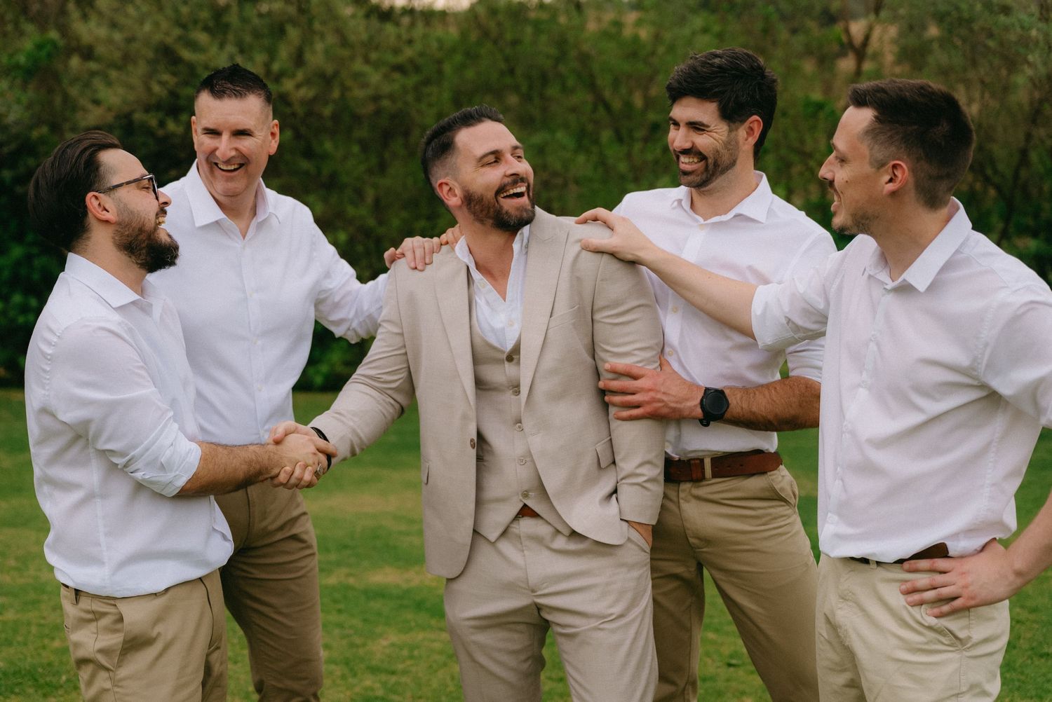 Groomsmen in tan suits celebrate with enthusiastic gestures outdoors.