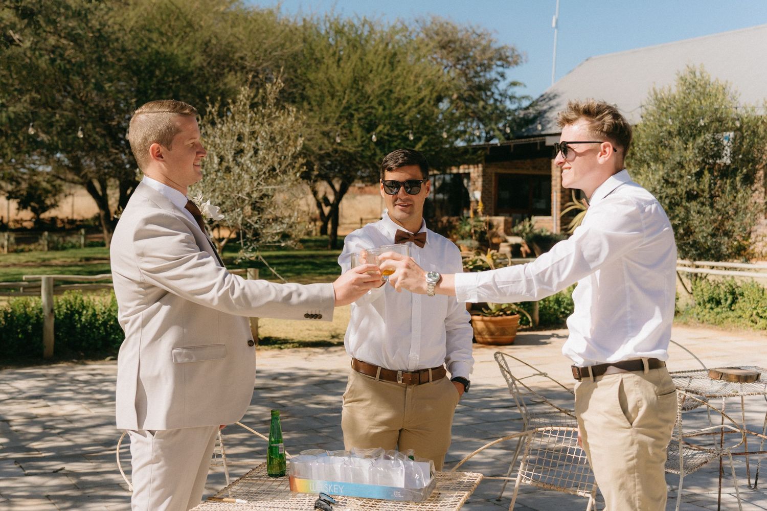 Wedding party members popping champagne bottles outdoors in celebration.