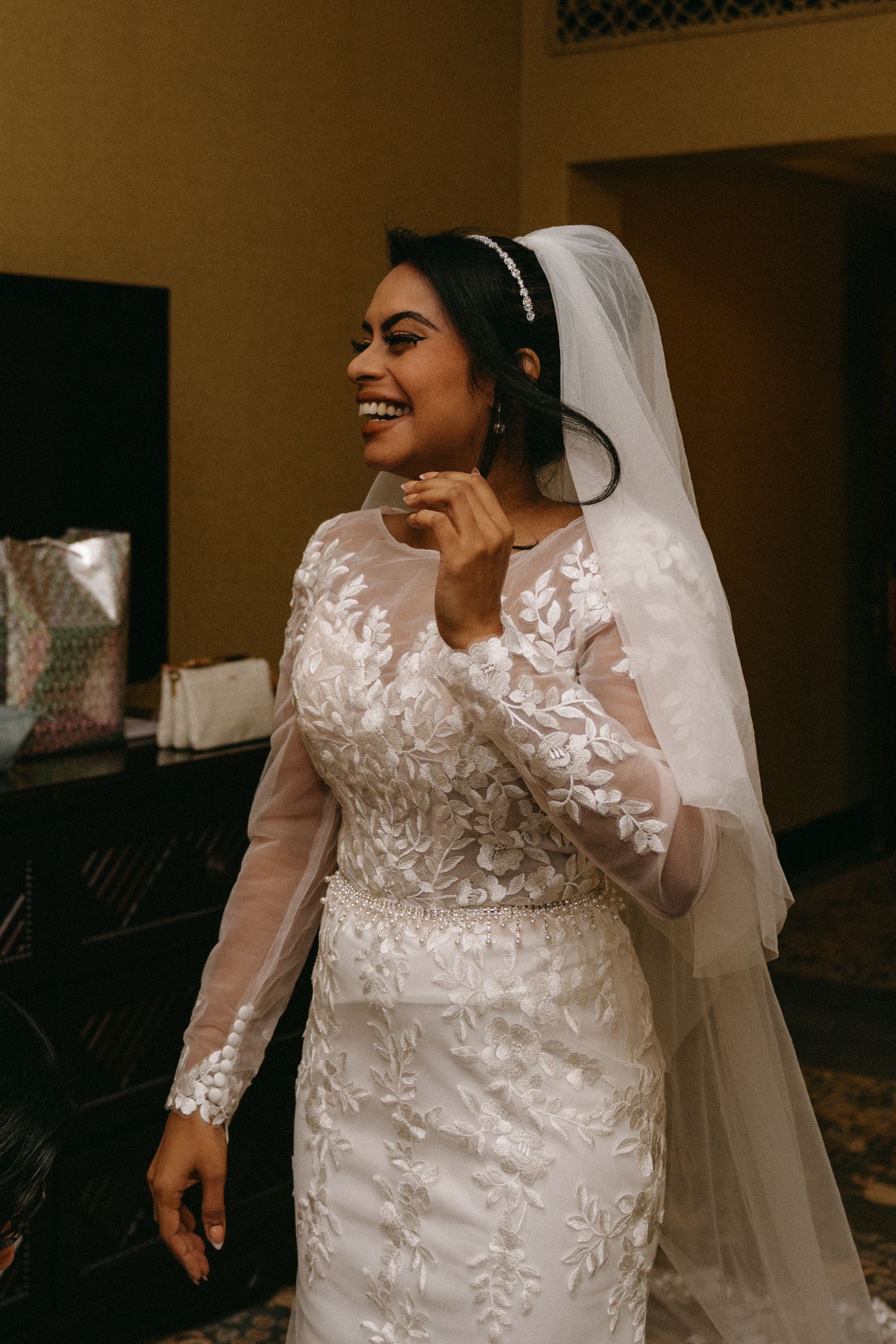 Bride in an elegant lace long-sleeve wedding gown with floral appliques and flowing veil poses during wedding photo session.