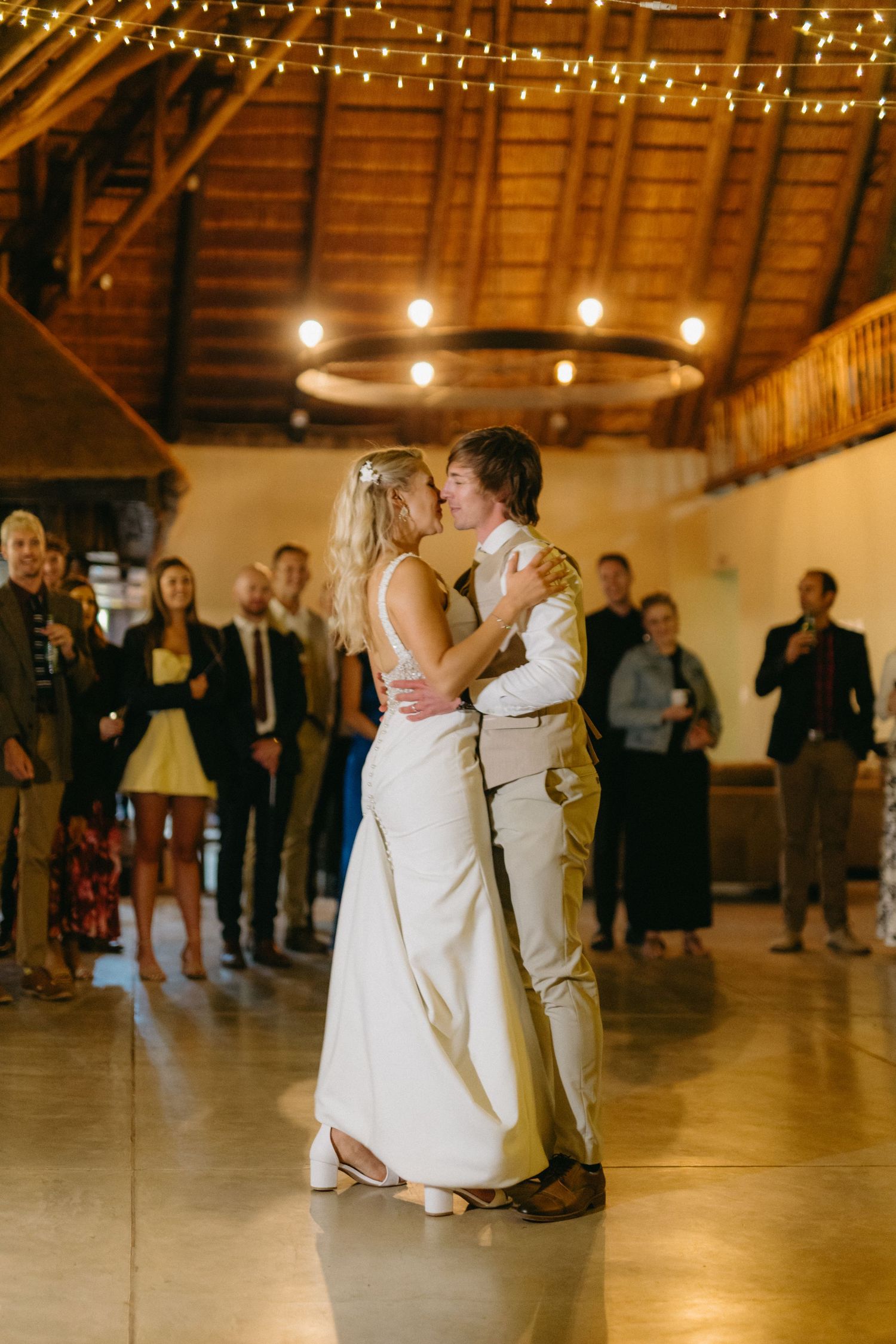 Couple shares their first dance under string lights in rustic barn reception venue.