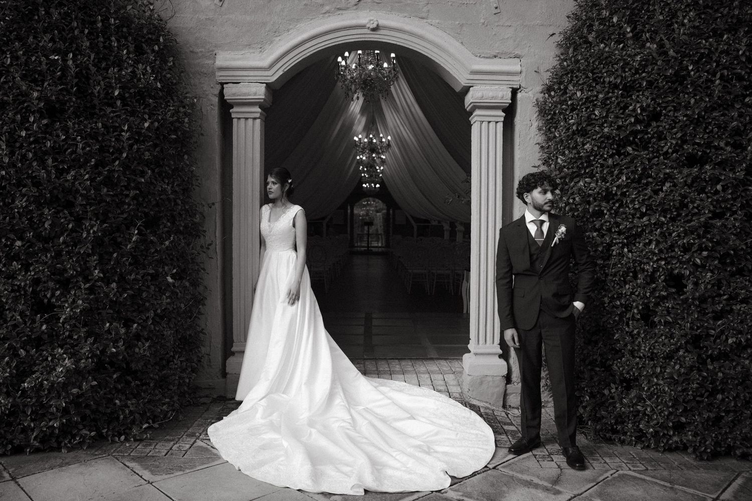 Black and white photo of a wedding couple standing in front of an ornate archway entrance.