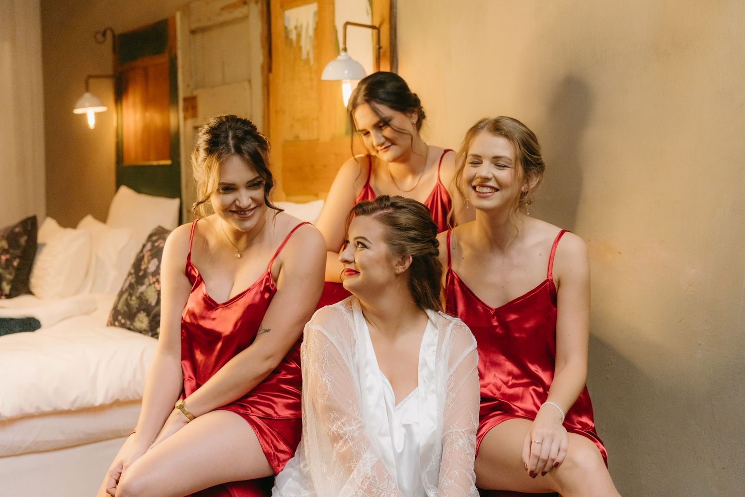 Bridal party in red dresses sharing joyful moment while getting ready.