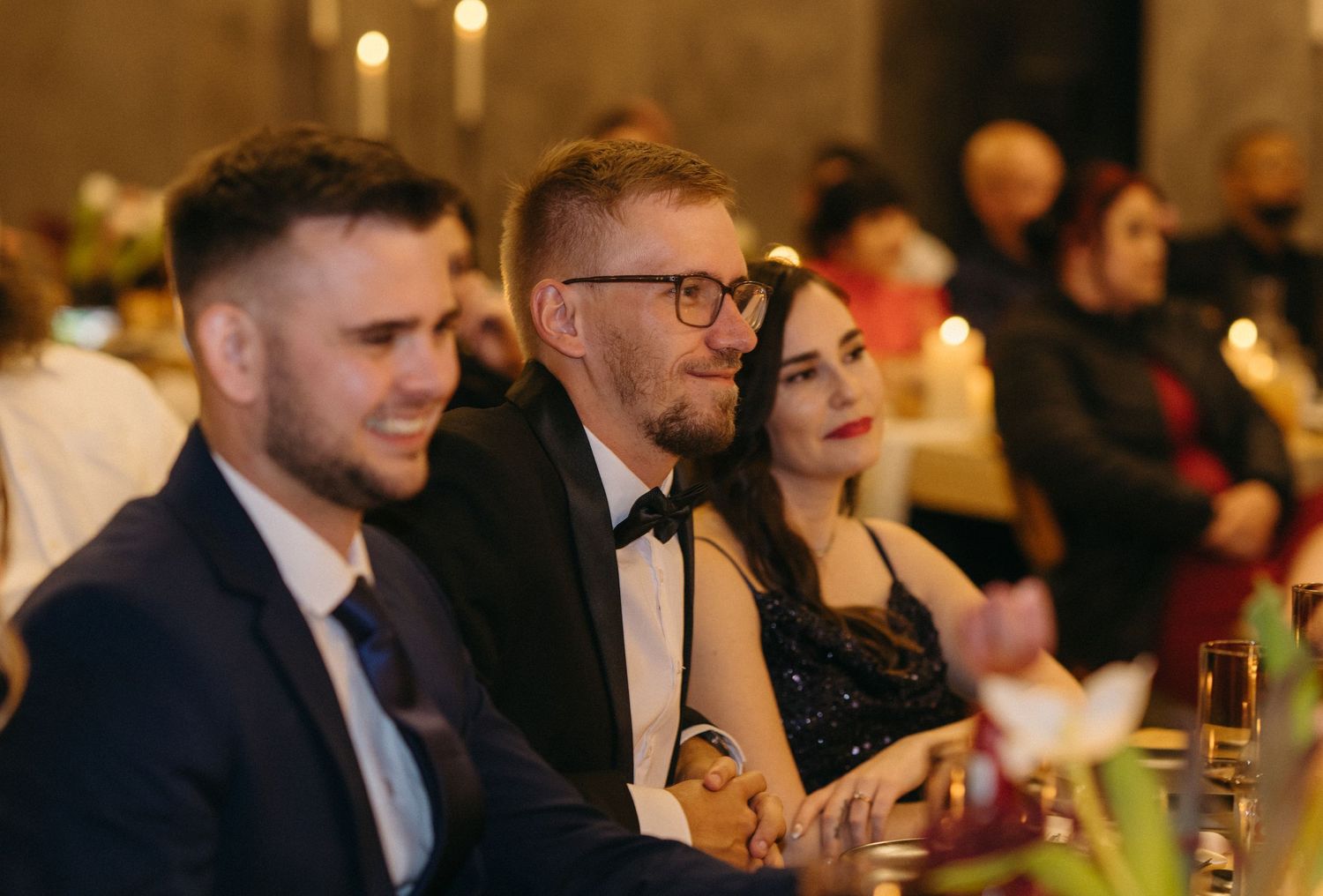 Wedding reception guests seated at tables with glowing candlelight and elegant decor.