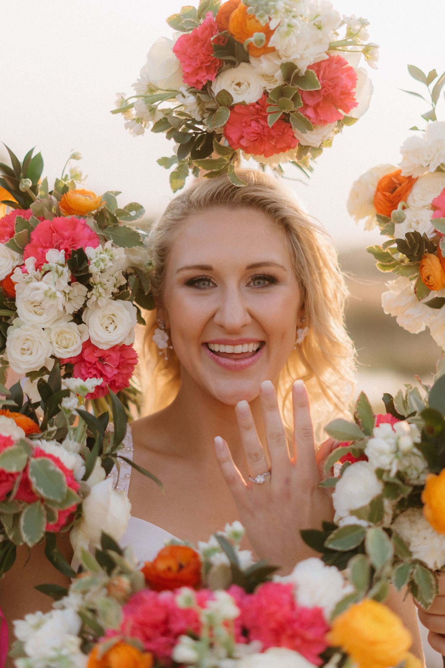 Beautiful floral arrangement frames a bridal portrait with pink and orange roses against a sunset backdrop.