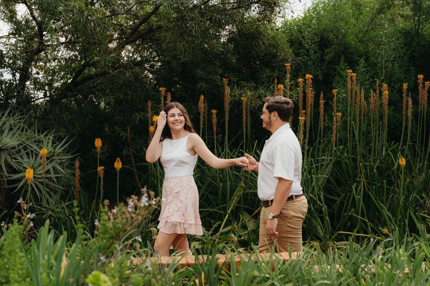 Couple holding hands and dancing among tall yellow flowers and lush green garden plants in Pretoria Botanical Gardens