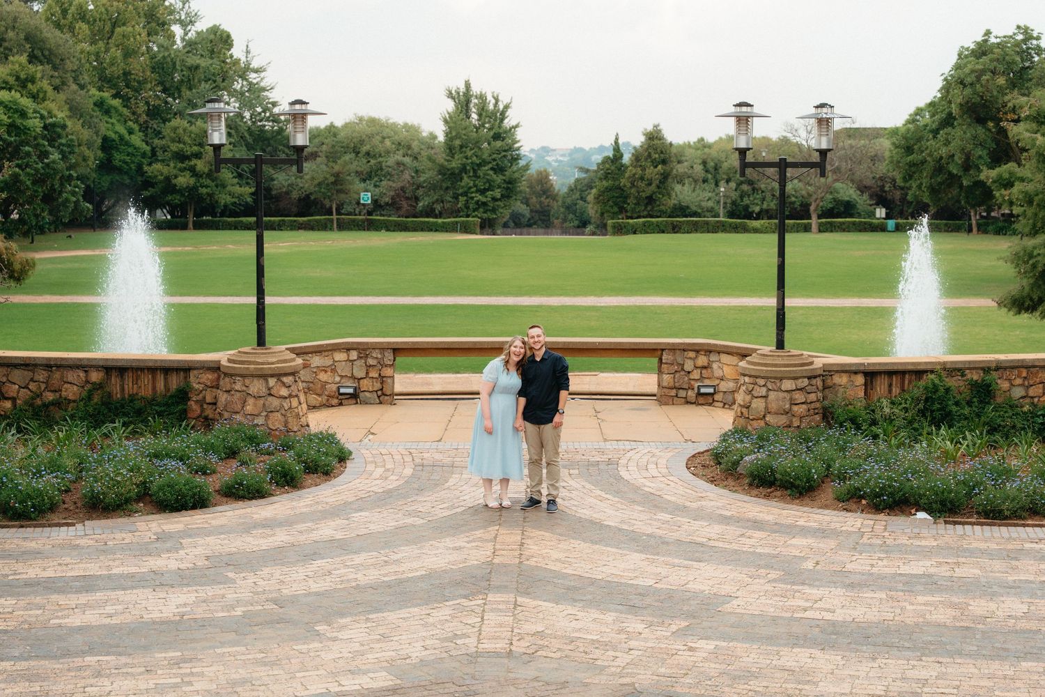 A panoramic view of a manicured park with fountains, pathways, and lush green lawns stretching across the landscape.