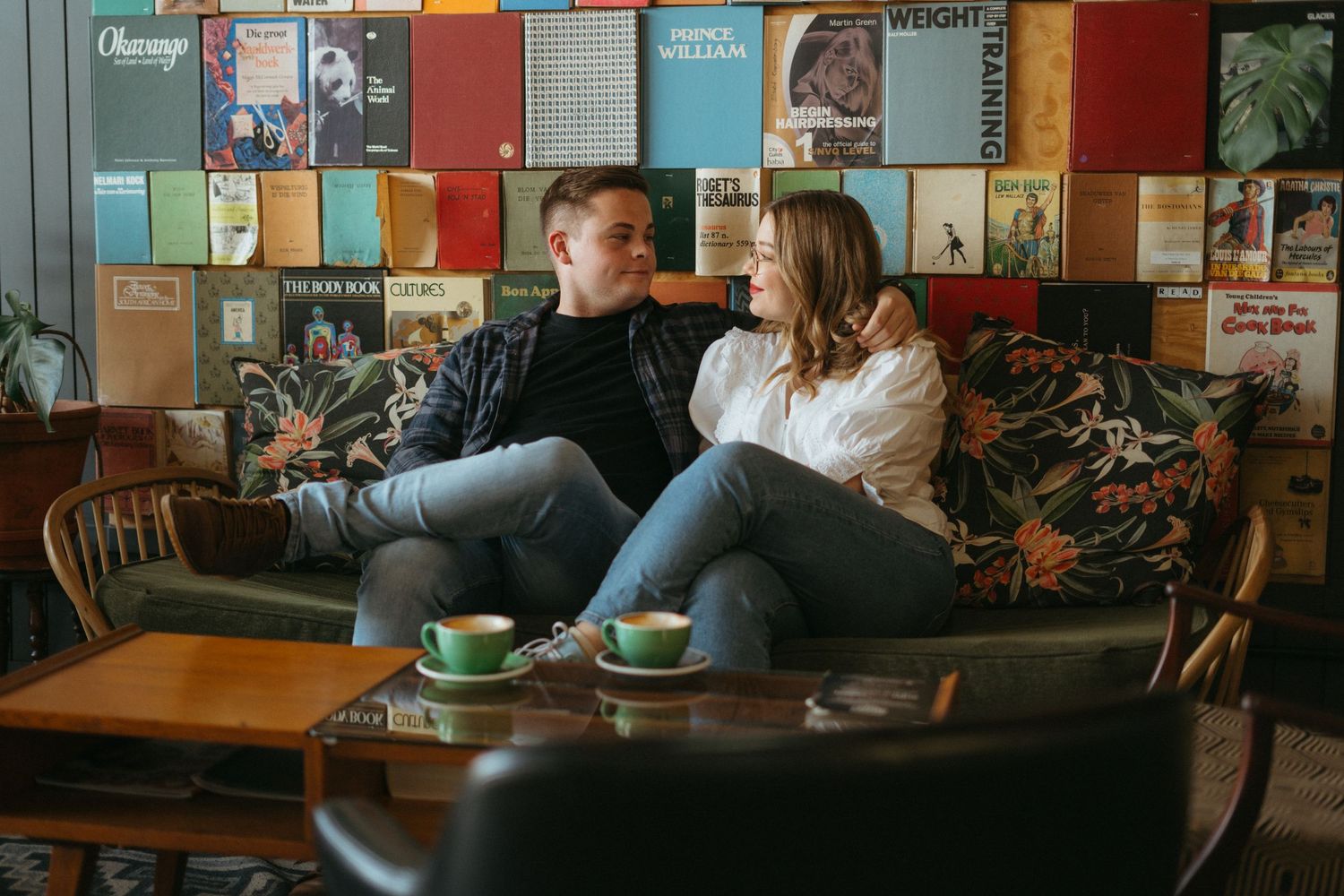 Two people relax on a couch at a coffee shop with colorful album covers and posters decorating the wall behind them.