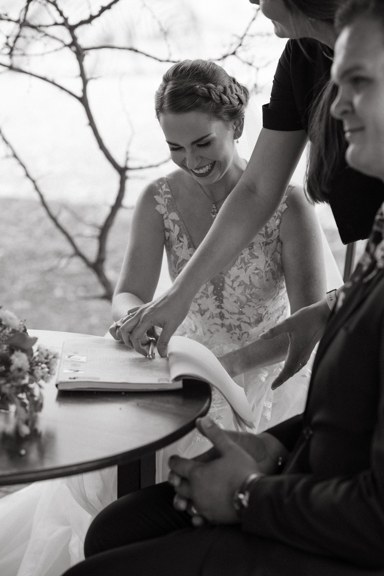 A black and white photo capturing the signing of wedding documents on a table.
