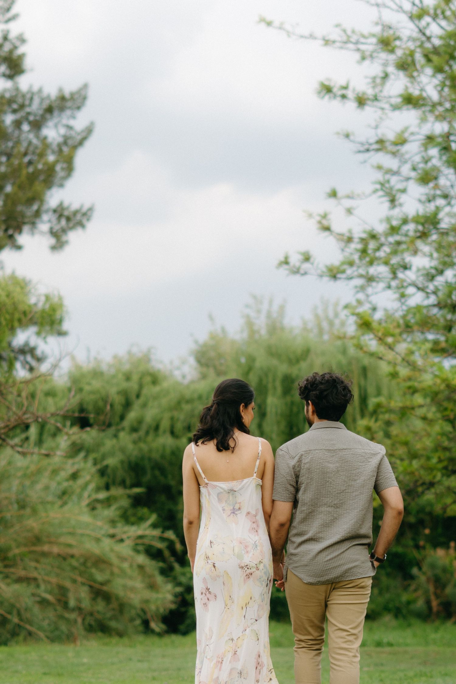 A couple walks together in a garden setting, viewed from behind against verdant scenery.