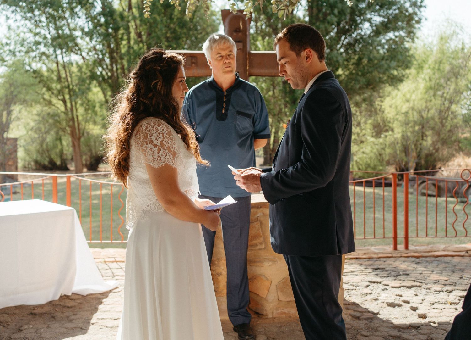 Outdoor wedding ceremony with couple and officiant standing beneath a rustic covered patio.