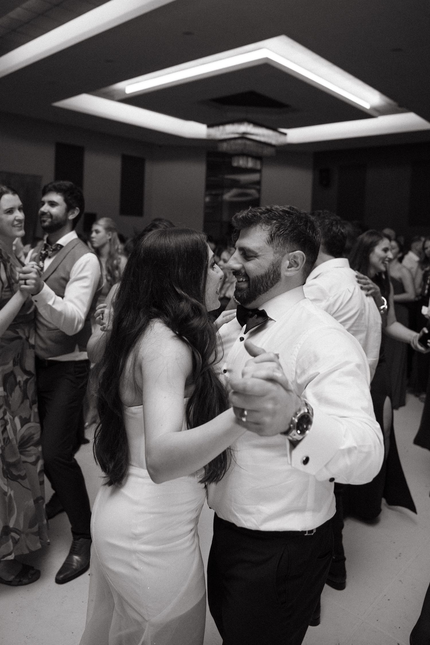 Black and white photo of a couple sharing a romantic dance at a wedding reception surrounded by guests.