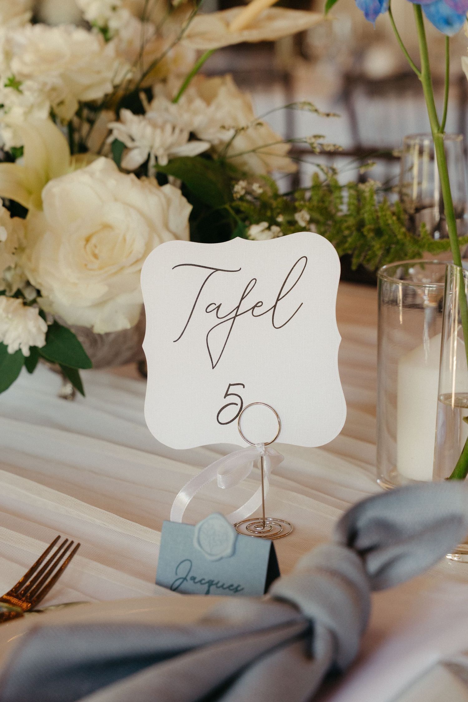Wedding table setting with handwritten place cards and blue accents against a white tablecloth.