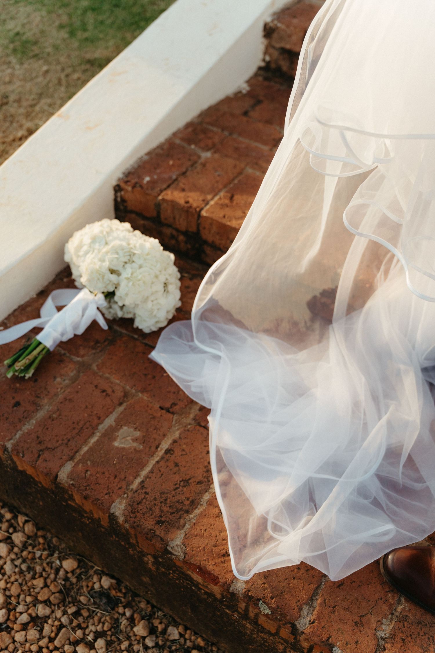 Delicate white wedding veil fabric drapes over red brick steps with small pebbles visible in the background.