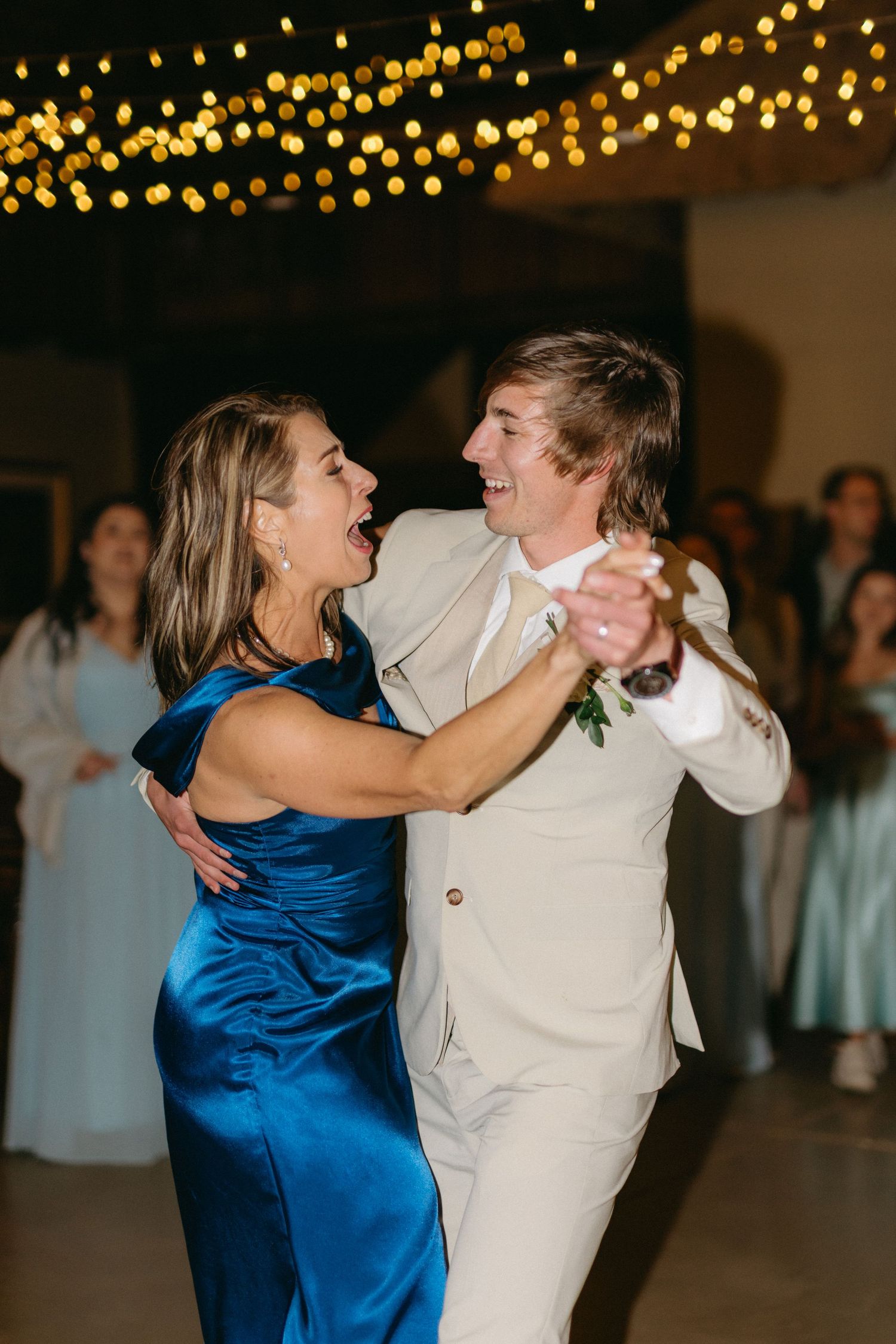 Dancers in blue and white attire moving gracefully under twinkling string lights at an evening celebration.