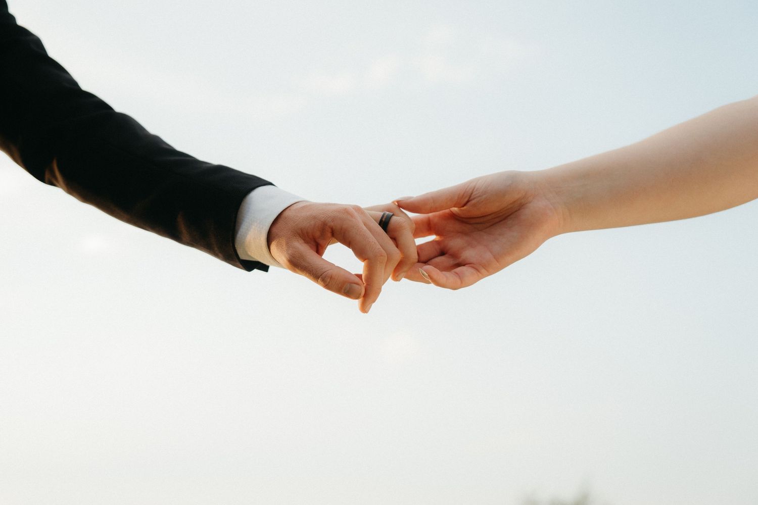 Close-up shot of two hands reaching towards each other against bright sky background.